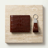Brown crocodile embossed Italian leather wallet and crocodile-patterned keychain corporate gift set on a beige stone surface
