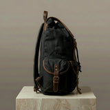 Black backpack with brown leather straps on a neutral background