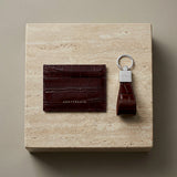 Burgundy leather cardholder and crocodile burgundy leather keychain on a beige stone surface