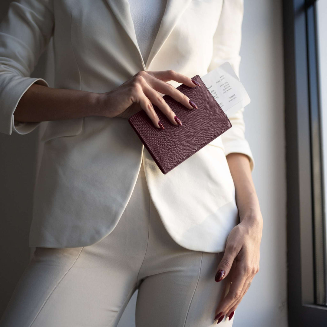 A burgundy lizard-embossed GENTCREATE passport holder held against a cream suit, a travel receipt inside