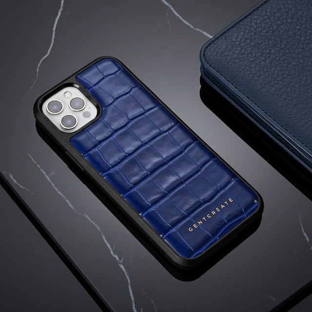 파란색 악어 패턴의 전화 케이스가 'GENTCREATE' 브랜드가 있는 어두운 표면에 놓여 있습니다.