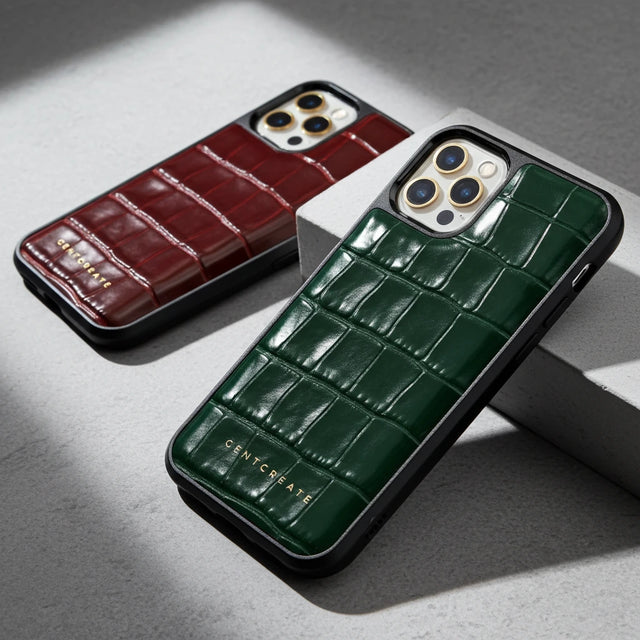 두 개의 전화 케이스, 하나는 갈색이고 하나는 녹색으로, 회색 표면에 악어 질감이 있습니다.