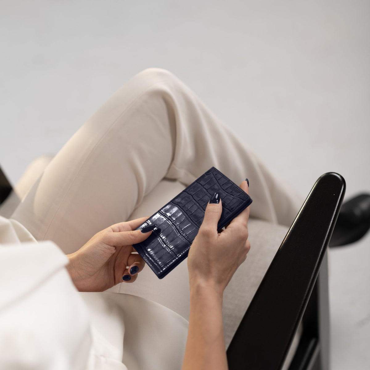 Two hands hold a navy crocodile-embossed GENTCREATE passport holder over a cream suit