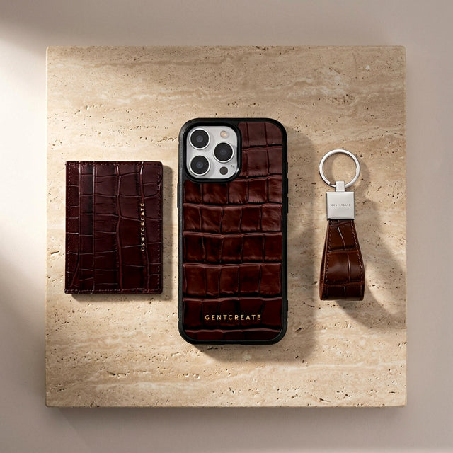 Burgundy crocodile-patterned leather iPhone case, wallet, and keychain by GENTCREATE on a beige stone surface