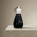 Black crocodile-embossed leather keychain with silver GENTCREATE logo on a beige surface