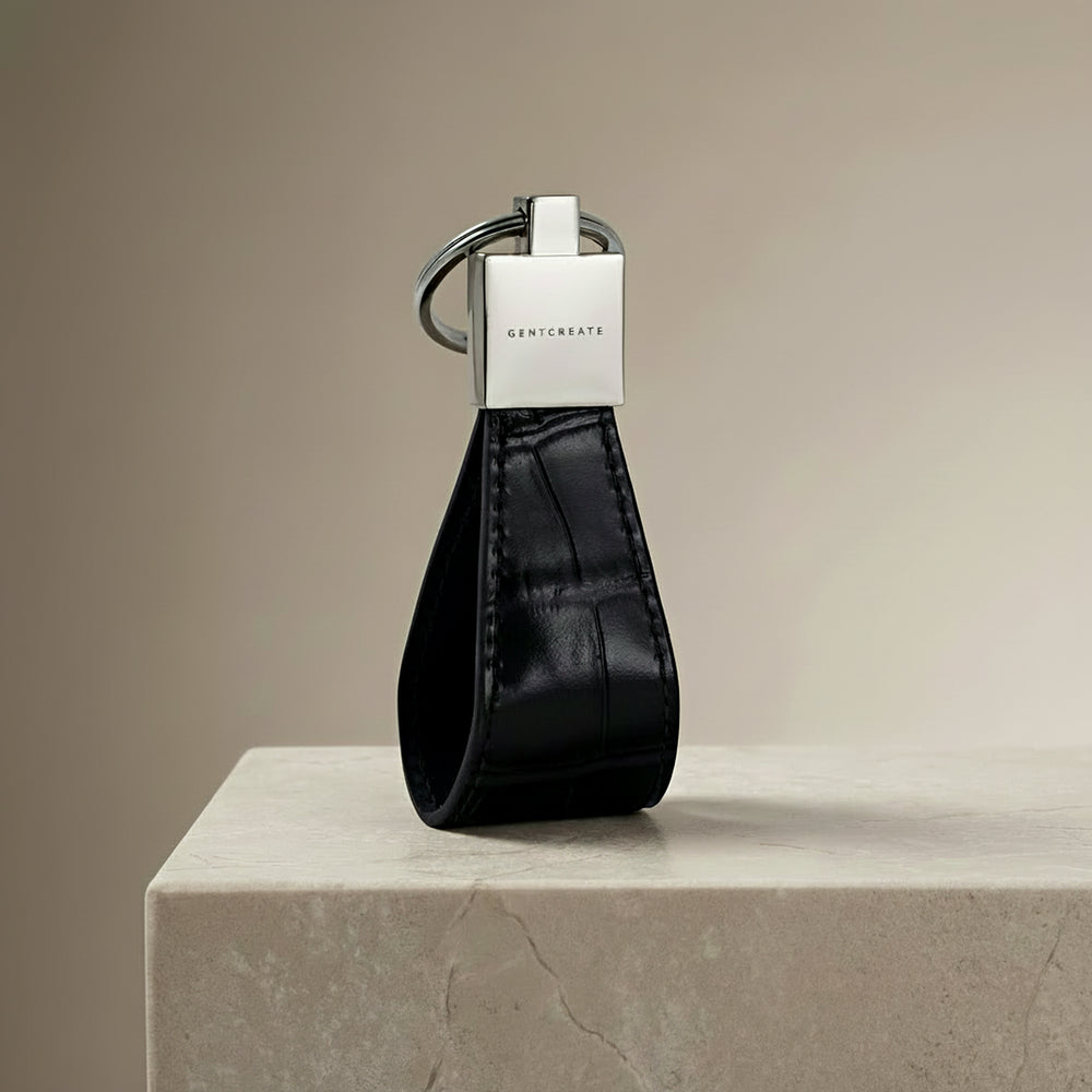 Black crocodile-embossed leather keychain with silver GENTCREATE logo on a beige surface