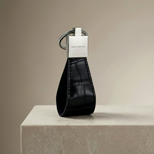 Black crocodile-embossed leather keychain with silver GENTCREATE logo on a beige surface