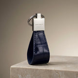 Blue leather keychain with silver tag on a beige surface