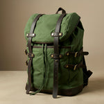 Green canvas backpack with leather straps on a beige background
