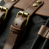 Close-up of canvas backpack brown leather straps with brass buckles on a black background