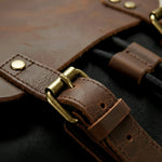 Close-up of a brown leather backpack with brass hardware on a dark background