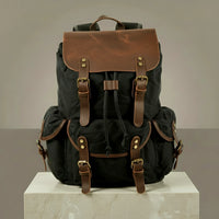 Black canvas and leather backpack with brown leather straps on a neutral background