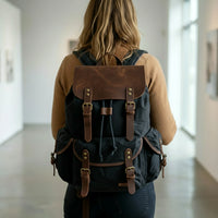 Person wearing a black canvas and leather backpack with brown leather straps in an indoor setting