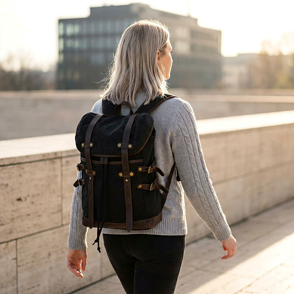 Person wearing a black canvas retro backpack by GENTCREATE walking on a bridge with buildings in the background