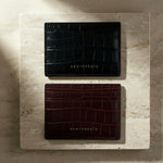 Two black and burgundy leather card holders on a marble surface with 'GENTCREATE' branding.