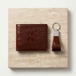 Brown crocodile embossed Italian leather wallet and crocodile-patterned keychain corporate gift set on a beige stone surface