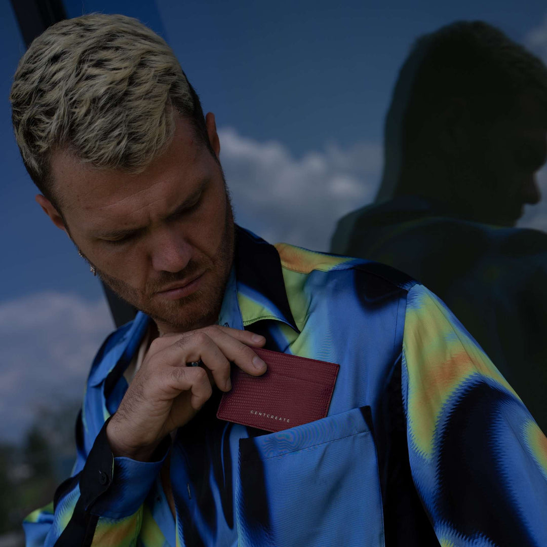 A man looks down as he slides a burgundy lizard-embossed GENTCREATE card holder into his shirt pocket
