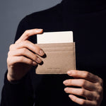 Close-up of hands holding a beige pebble leather card holder by GENTCREATE with a card in the top slot