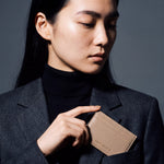 Woman slipping a beige pebble leather card holder by GENTCREATE into a blazer chest pocket