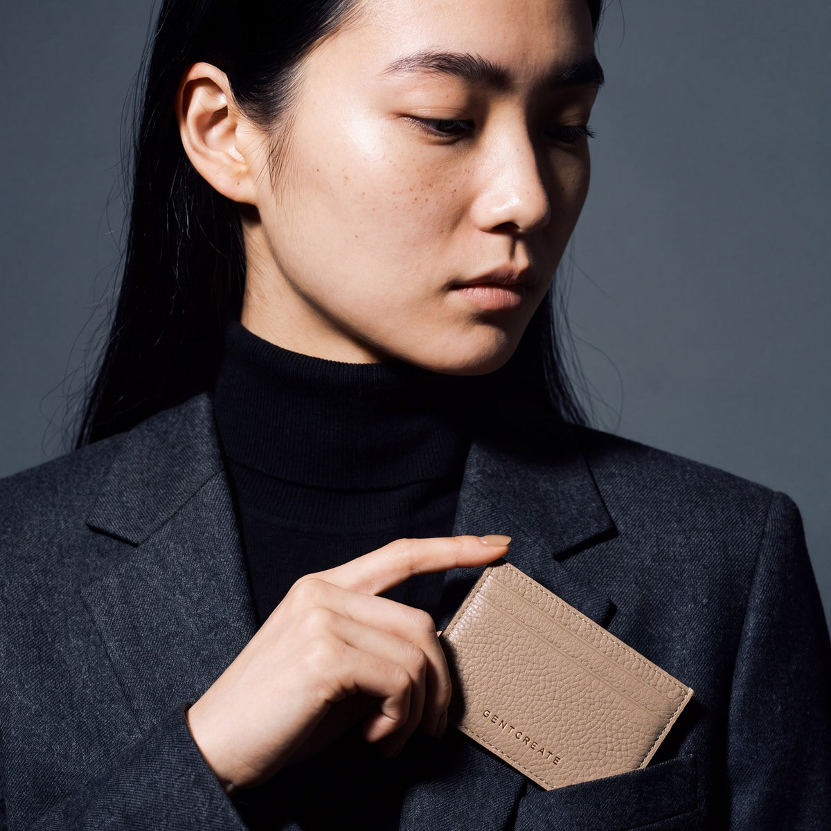 Woman slipping a beige pebble leather card holder by GENTCREATE into a blazer chest pocket