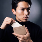 Man holding a slim beige pebble leather card holder by GENTCREATE and drawing out a card