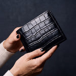 Close-up of hands holding a black crocodile-embossed leather bifold wallet by GENTCREATE