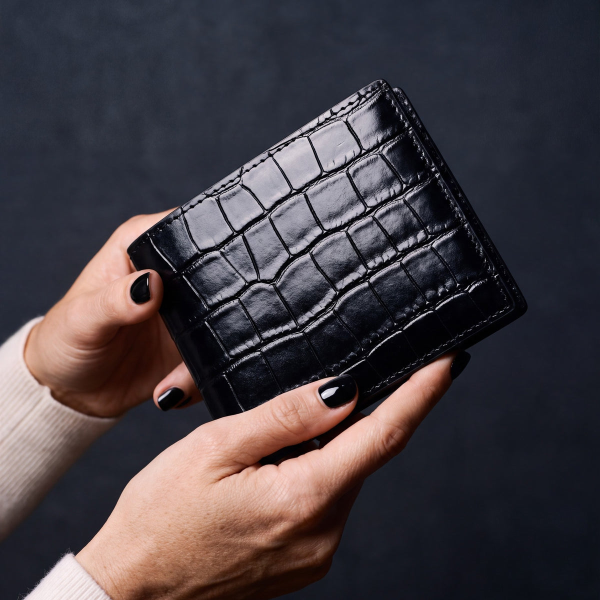 Close-up of hands holding a black crocodile-embossed leather bifold wallet by GENTCREATE