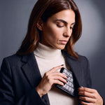 Woman sliding a black crocodile-embossed leather bifold wallet by GENTCREATE into a blazer pocket