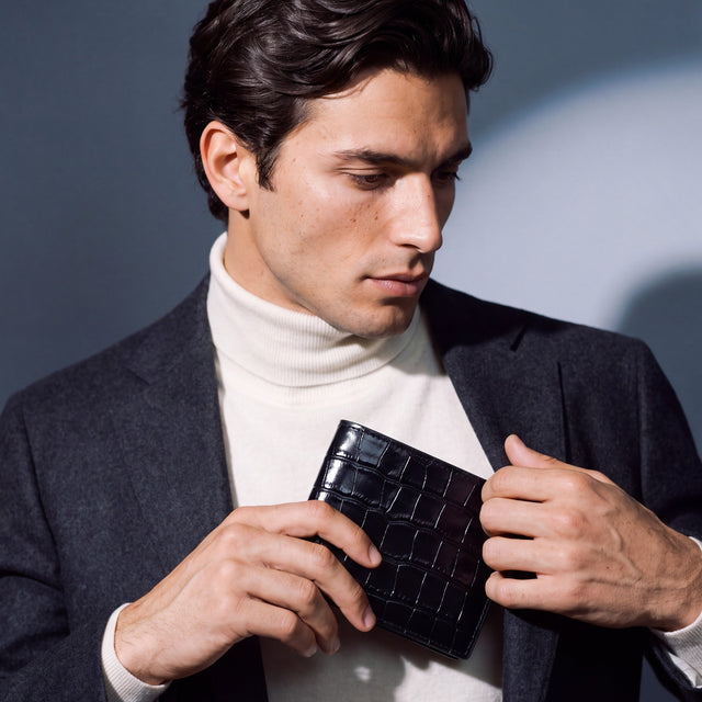 Man sliding a black crocodile-embossed leather bifold wallet by GENTCREATE into a blazer pocket