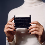 Close-up of hands holding a black crocodile-embossed leather card holder by GENTCREATE with a card in the top slot