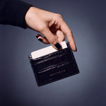 Hand placing a card into a black crocodile-embossed leather card holder by GENTCREATE