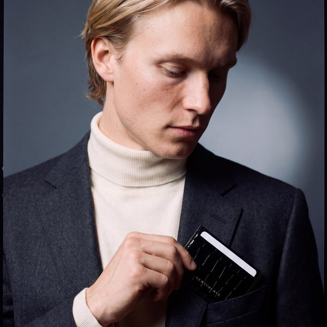 Man slipping a black crocodile-embossed leather card holder by GENTCREATE into a blazer chest pocket