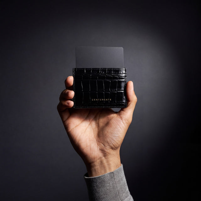 Man's hand holding a black crocodile-embossed leather card holder by GENTCREATE with a card in a dark studio