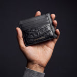 Männerhand hält ein schwarzes Kartenetui aus Leder mit Krokoprägung und Außenfächern von GENTCREATE im dunklen Studio
