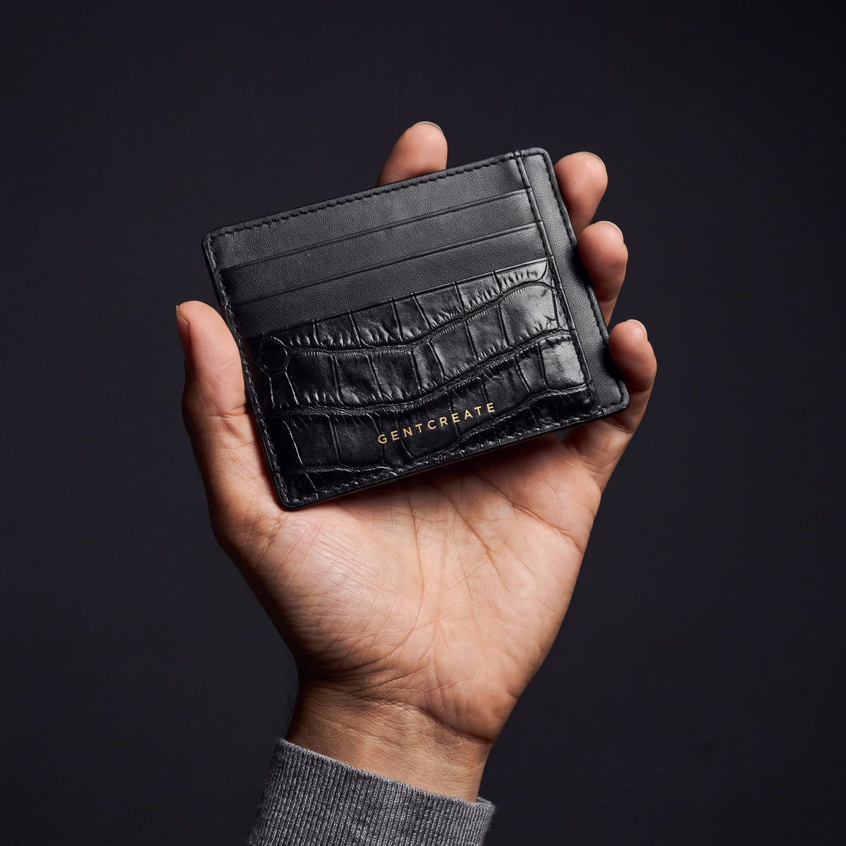 Männerhand hält ein schwarzes Kartenetui aus Leder mit Krokoprägung und Außenfächern von GENTCREATE im dunklen Studio