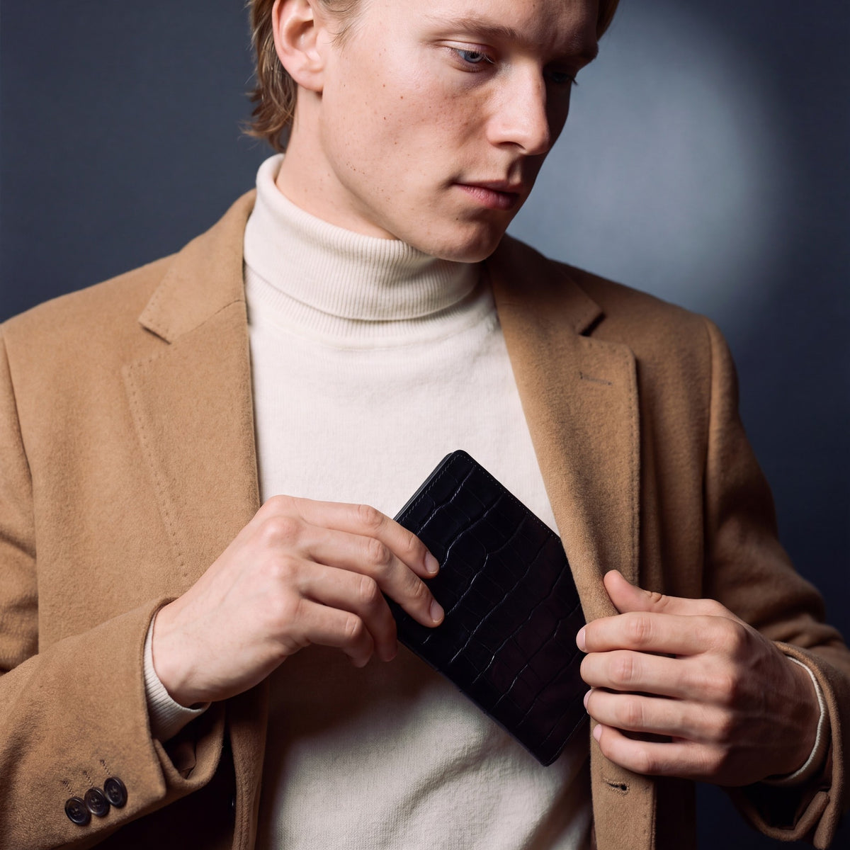 Man tucking a black crocodile-embossed leather passport holder by GENTCREATE into his coat