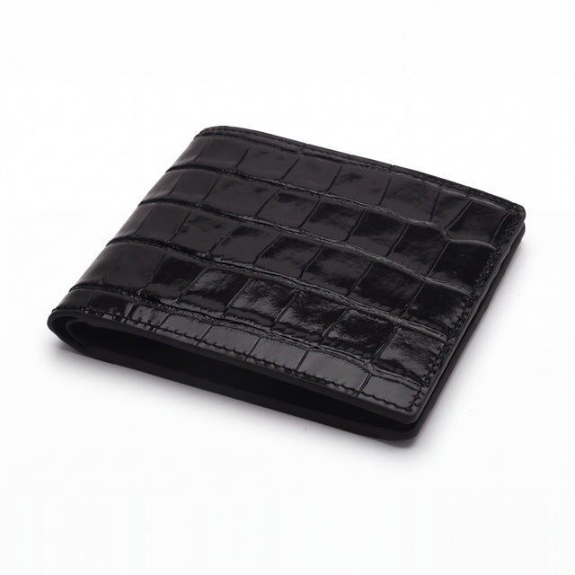 Closed black glossy crocodile-embossed leather bifold wallet by GENTCREATE lying on white