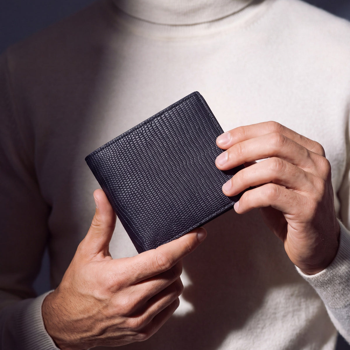 Close-up of hands holding a black lizard-embossed leather bifold wallet by GENTCREATE