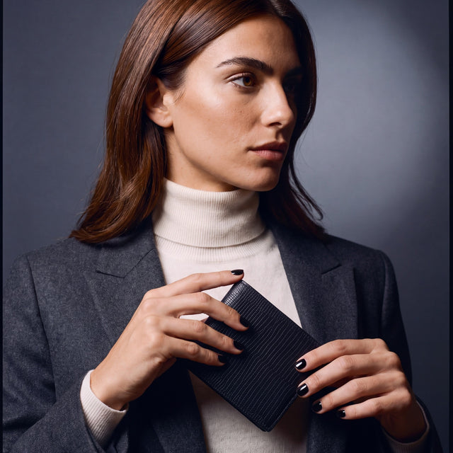Woman sliding a black lizard leather bifold wallet by GENTCREATE into a blazer pocket
