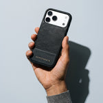 Hand holding a black lizard-embossed leather iPhone 18 Pro Max case by GENTCREATE against pale grey
