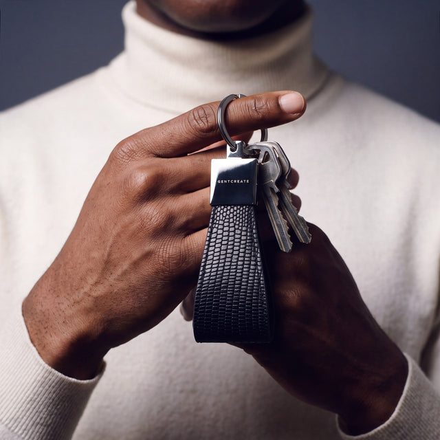 Close-up of a black lizard-embossed leather keychain by GENTCREATE with house keys hanging from a finger