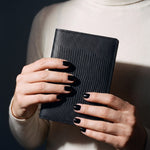 Close-up of hands holding a black lizard-embossed leather passport holder by GENTCREATE