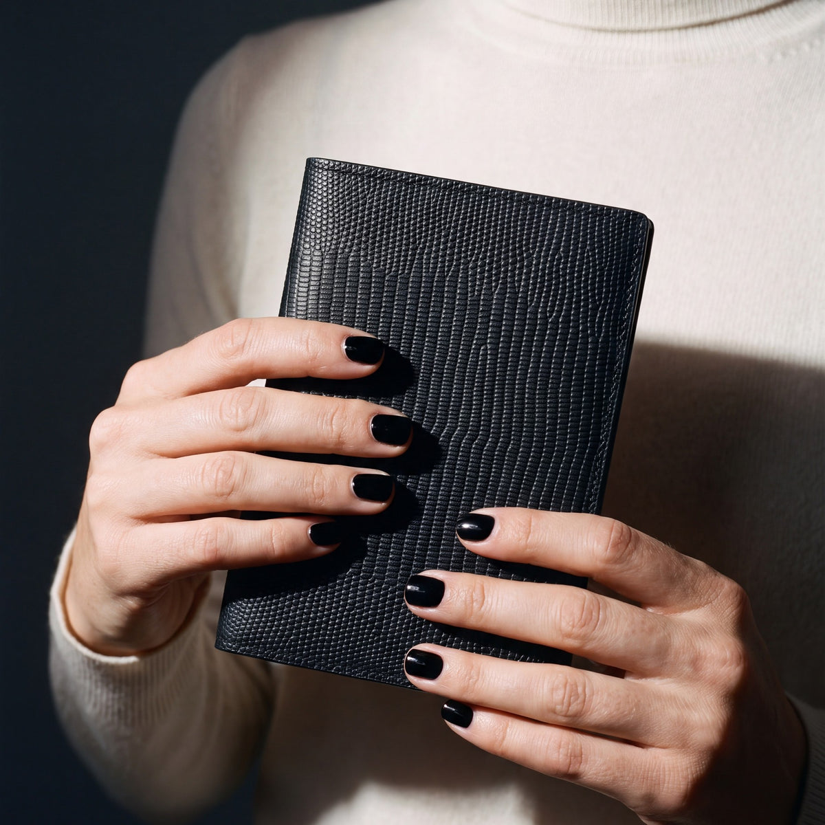 Close-up of hands holding a black lizard-embossed leather passport holder by GENTCREATE