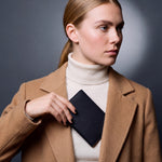 Woman holding a black lizard-embossed leather passport holder by GENTCREATE against her coat