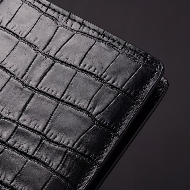 Close-up of the matte crocodile-embossed tiles and stitched corner of a black bifold wallet by GENTCREATE