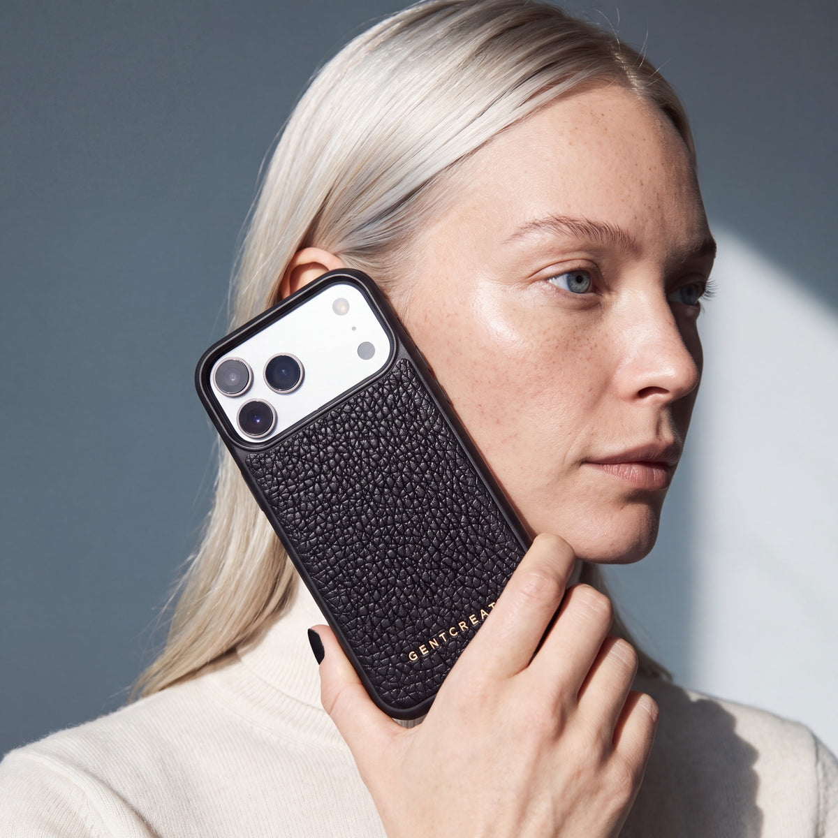 Kvinde holder et sort iPhone 18 Pro Max-cover i narvet kalveskind fra GENTCREATE ved siden af ansigtet i dagslys fra et vindue