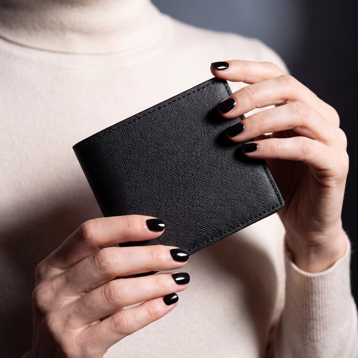 Close-up of hands holding a black Saffiano leather bifold wallet by GENTCREATE