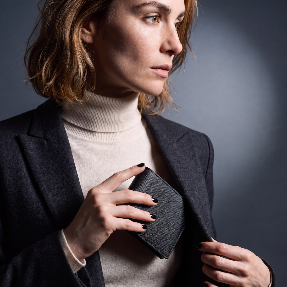 Woman sliding a black Saffiano leather bifold wallet by GENTCREATE into a blazer pocket