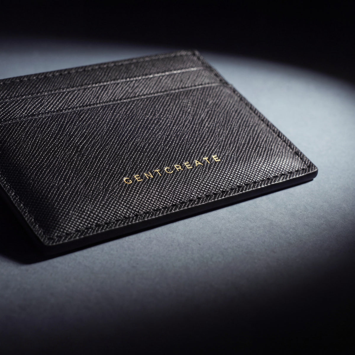 Close-up of the gold GENTCREATE stamp pressed into a black Saffiano leather card holder