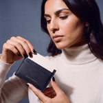 Woman holding a slim black Saffiano leather card holder by GENTCREATE and drawing out a card